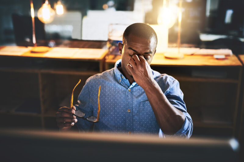 A man pinching the bridge of his nose at work.